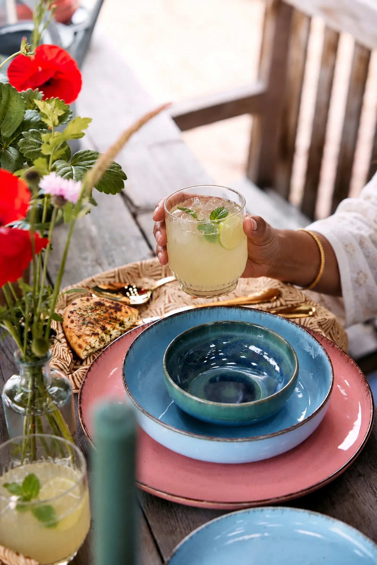 South Indian hands holding a nannari-lime cooler above stacked glazed dinnerware.