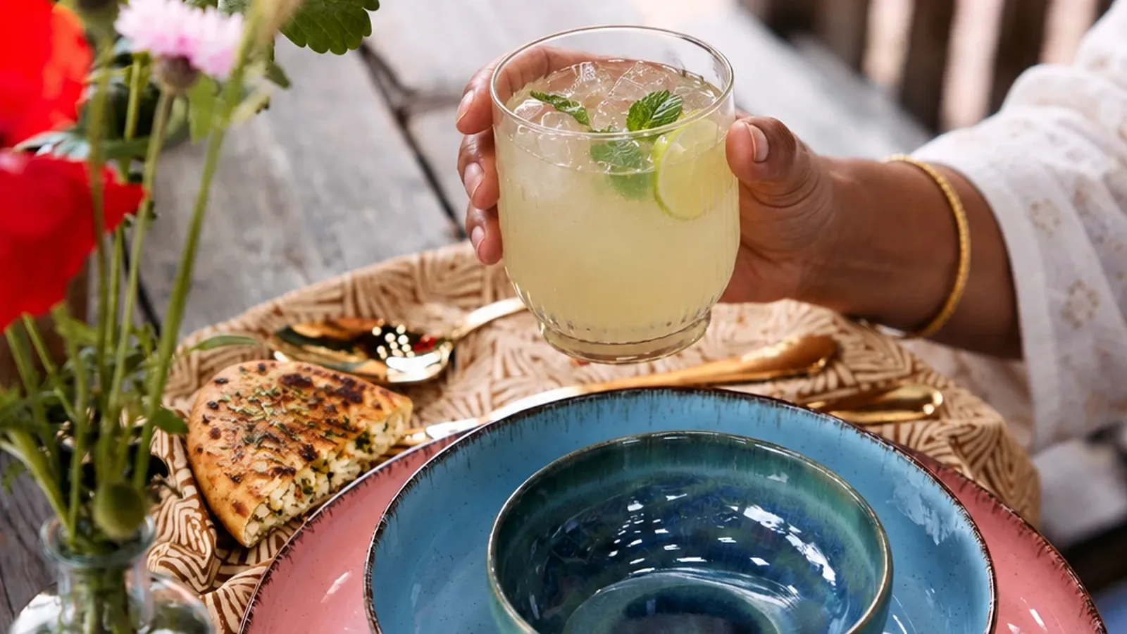 South Indian hands holding a nannari-lime cooler above stacked glazed dinnerware.